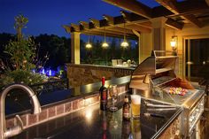 an outdoor grill with lights and bottles on the counter top at night, next to a patio