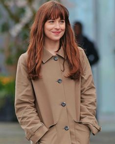 a woman with long red hair is wearing a trench coat and smiling at the camera