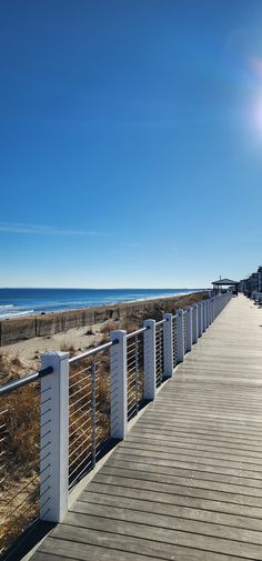 a wooden walkway leading to the beach with white railings on both sides and blue sky above