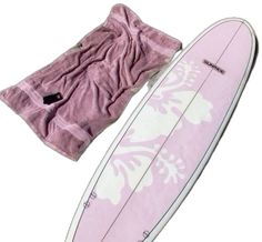 a pink surfboard laying on its side next to a purple and white towel with the bottom rolled up