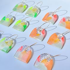 six pairs of earrings with different colors and designs hanging from silver hooks on a white surface