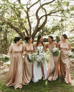 bridesmaids laughing together in front of a tree at their outdoor wedding ceremony with greenery and white flowers