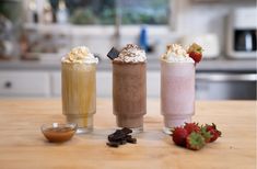 three different drinks sitting on top of a wooden table next to strawberries and chocolate