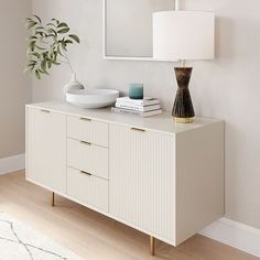 a white sideboard with a mirror and vase on top next to a table lamp