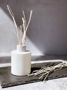 a white vase sitting on top of a table next to some branches in the corner