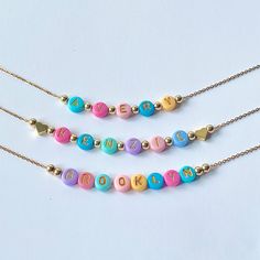 Add a burst of vibrant charm to your little one's outfit with our Bright Colorful Beads Name Necklace! This delightful piece combines the timeless elegance of dainty gold name beads with an array of eye-catching, colorful hued beads. Each letter of your child's name is lovingly crafted with precision and adorned with a captivating spectrum of colors, creating a personalized gift that will surely bring smiles. These necklaces would also make great party favors for a childs birthday party. Beads are chosen randomly and the necklace is accented with 18K gold hearts or 18K round ball beads.  Necklace chain is 18K plated and dainty.  Choose which style you would like from the drop down menu along with the length of the necklace. Necklace is packaged for gift giving. To see more Kids Necklaces c Adjustable Colorful Beads Necklace For Valentine's Day, Valentine's Day Multicolor Beaded Necklaces, Cute Multicolor Jewelry With Heart Beads, Cute Personalized Multicolor Charm Necklaces, Cute Multicolor Heart Beads Jewelry, Playful Beaded Charm Necklaces For Gifts, Playful Beaded Charm Necklaces As Gifts, Playful Beaded Charm Necklace For Gifts, Adjustable Playful Beaded Necklaces With Tiny Beads