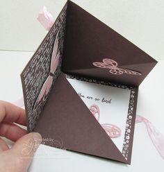 a hand is holding an origami box with a bow on the front and side