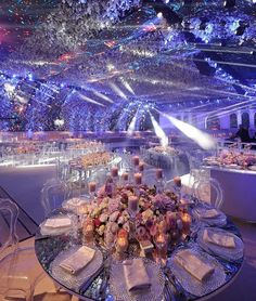 a table set up for an event with candles and flowers in the center, surrounded by blue lights