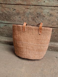 "Unique and stylish natural sisal kiondo bag with stitched leather straps. Ideal as a beach bag, shopping basket, market basket or storage basket. This unique tote bag is handmade by a group of ladies in a remote rural village in Machakos, Kenya. Do not clean with water. If the bag gets wet, please dry to avoid dampness.  Leather type used is bovine, from cattle. It's natural and in it's purest form. DIMENSIONS Bottom width: 10\"/25.5cm Top width: 14\"/35.56cm Depth: 10\"/25.5cm Straps: 15\"/38cm SHIPPING All orders ship via DHL Express (3-5) days delivery time." Natural Jute Bucket Bag With Braided Handles, Woven Natural Fiber Basket Bucket Bag, Natural Woven Straw Tote Bag, Woven Basket Bucket Bag In Natural Color, Natural Woven Basket Bucket Bag, Casual Natural Basket Bag, Casual Natural Color Basket Bags, Casual Brown Palm Leaf Bag, Casual Natural Fiber Basket Bag