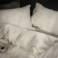 an unmade bed with white sheets, pillows and a magazine on the pillowcase