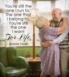 an older couple embracing each other in front of a window with a quote on it