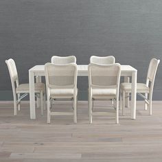 a white table and six chairs in front of a gray wall with wood flooring