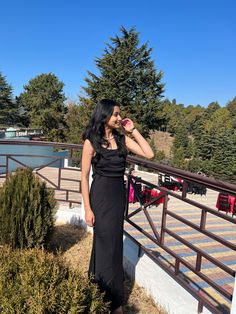 a woman in a black dress standing on a bridge drinking from a pink drink bottle