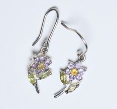 "Pair of silver tone metal earrings in a flower shape with round cut amethyst stones as petals, and a round cut citrine in the center. The leaves of the flower are marquise cut peridot. NOTE: One of the peridot is missing. 1 1/4 x 5/16\" 2.4g total UNMARKED" Silver Gemstone Flower Earrings, Silver Flower Gemstone Earrings, Warwick Ny, Amethyst Stones, Metal Earrings, Marquise Cut, Amethyst Stone, Flower Shape, Silver Diamonds