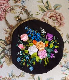 a black purse with flowers on it sitting on top of a floral print table cloth