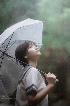 a young boy holding an umbrella while standing in the rain with it's eyes closed