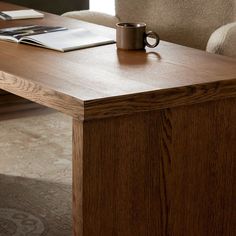 a coffee cup sitting on top of a wooden table next to a book and pen