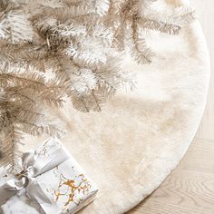 a white christmas tree skirt with a gift wrapped in silver foil and a bow on it