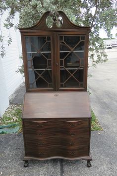 an old wooden desk with glass doors on it's top and bottom drawers, sitting in front of a tree