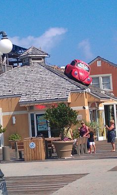 a red car is on top of the roof of a building and people are walking around