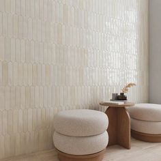 two round stools sitting next to each other in front of a white tiled wall