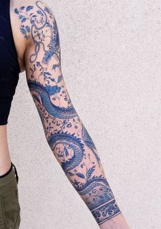 a woman with a dragon tattoo on her arm and leg is standing in front of a wall