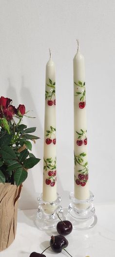 two candles with cherries on them next to some flowers