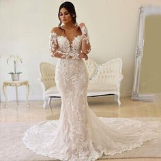 a woman standing in front of a mirror wearing a wedding dress with long sleeves and an open back