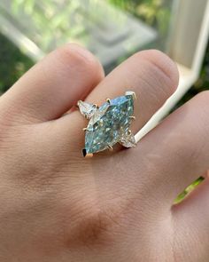 a person's hand holding a ring with an aqua blue stone in it and two white diamonds on the side