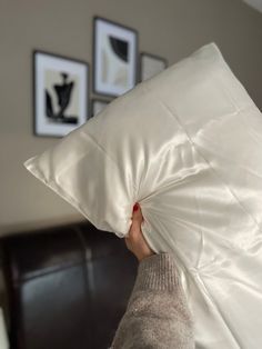 a person holding a white pillow in their hand with pictures on the wall behind them