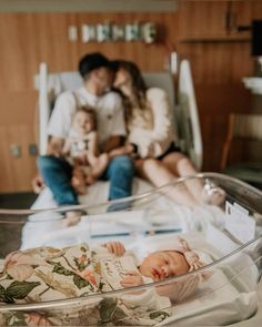 a man and woman sitting on a bed next to a baby in a glass bowl