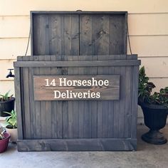 a large wooden box sitting on the side of a building next to potted plants