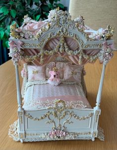 a dollhouse bed with pink and gold decorations on it's sides, sitting on a wooden table