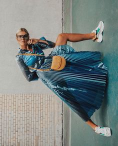 a woman leaning against a wall with her legs spread out and holding a tennis racquet