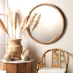 a round mirror hanging on the wall next to a chair and vase with dry grass in it