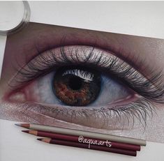 a pencil drawing of an eye with long lashes and brown eyeshade next to some colored pencils