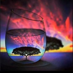 a fish bowl filled with water and a tree in the middle, under a colorful sky