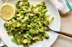 a white plate topped with broccoli next to a slice of lemon wedges