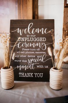 two vases filled with dried flowers sitting next to a sign that says welcome to our unplugged enemy