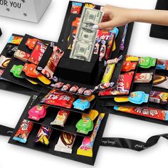 a person is grabbing money out of a box filled with candy bars and candies