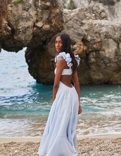 a woman standing on top of a sandy beach next to the ocean wearing a blue and white dress