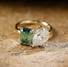 an emerald and diamond ring sitting on top of a wooden table