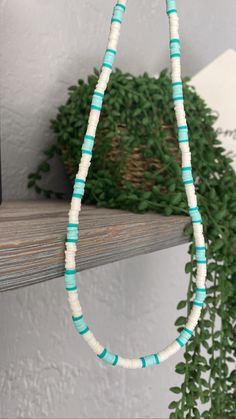 a blue and white beaded necklace hanging from a wooden shelf next to a potted plant