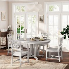 a white table and chairs in a room with wooden floors, windows, and rugs on the floor