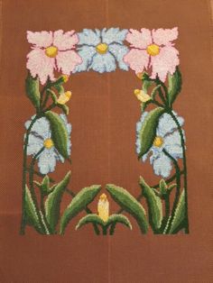 a cross stitched picture with flowers and leaves on brown background, in the shape of a frame