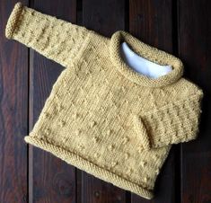 a knitted sweater sitting on top of a wooden floor next to a white bowl