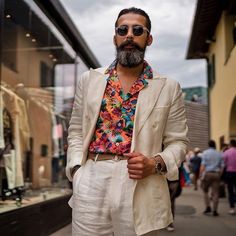 a man with a beard wearing sunglasses and a floral shirt is standing in front of a store