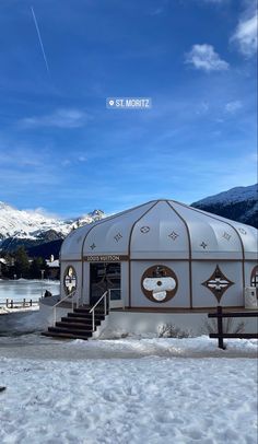 a small white building sitting on top of snow covered ground next to a mountain range