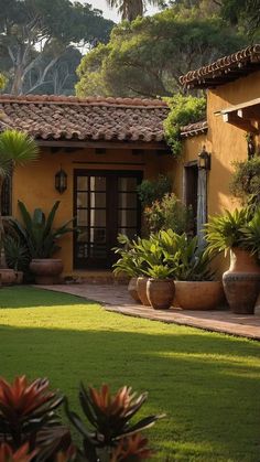 a yellow house with potted plants on the front lawn and trees in the background