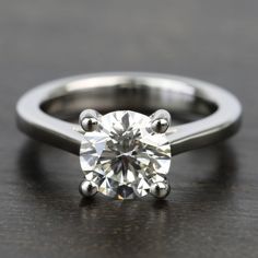 an engagement ring with a round brilliant cut diamond set in the shans, on a wooden surface